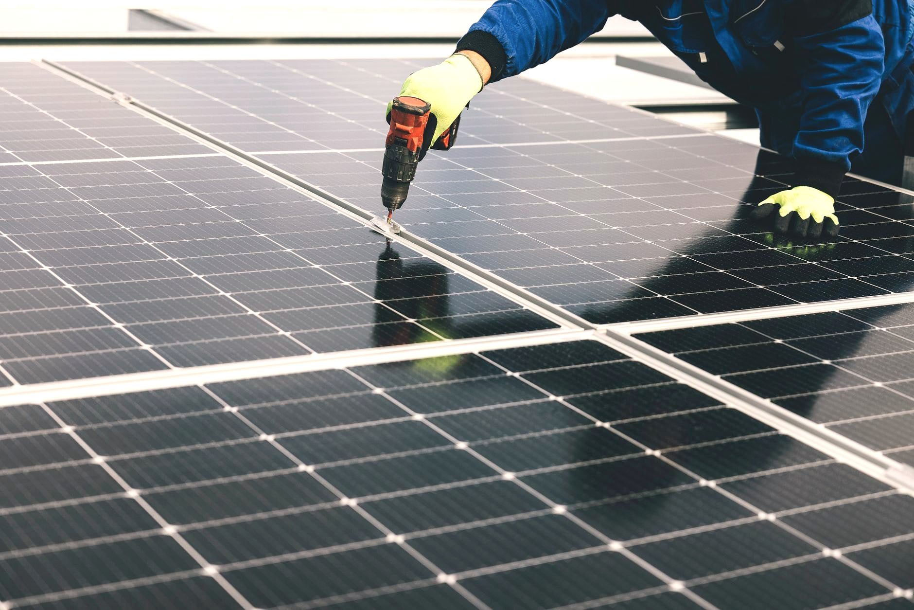 Technician drilling solar panel with cordless drill, gloved hands