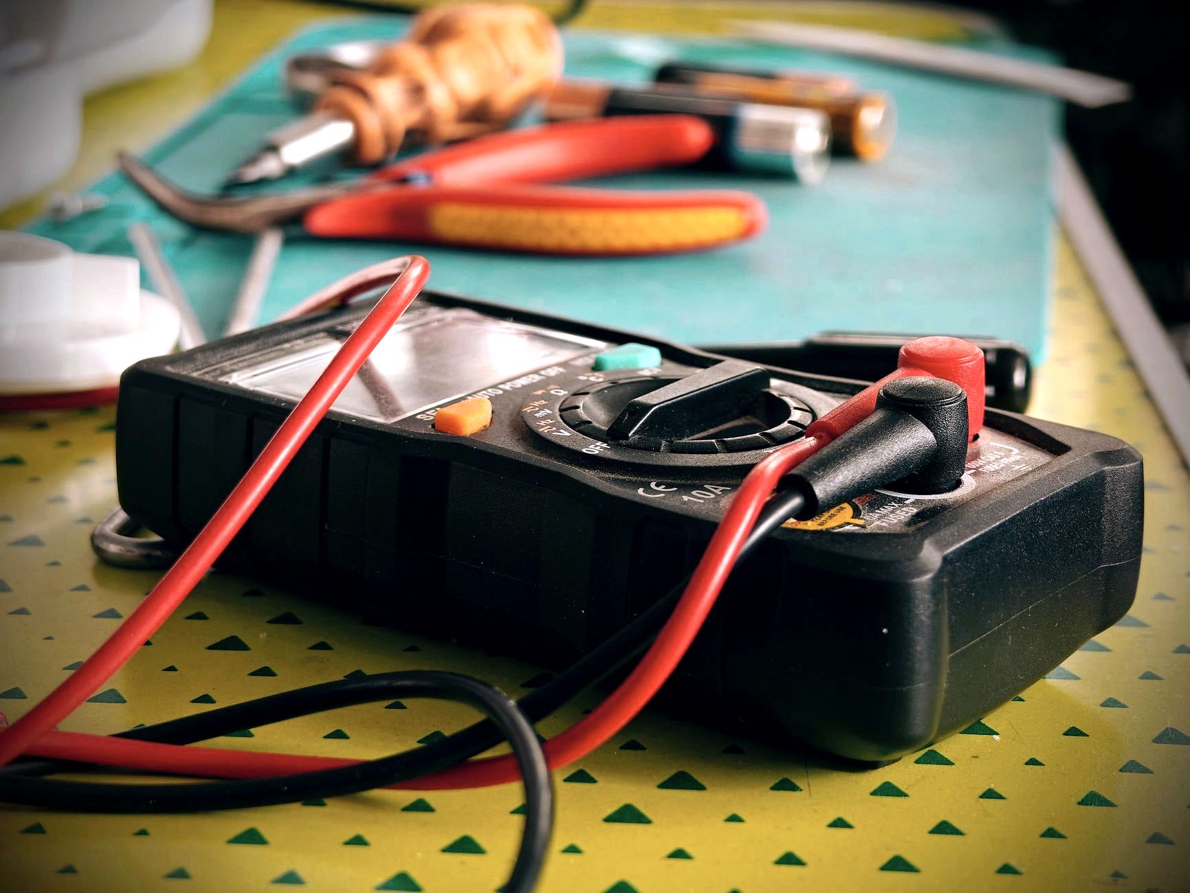 Multimeter with red leads and pliers on a workbench