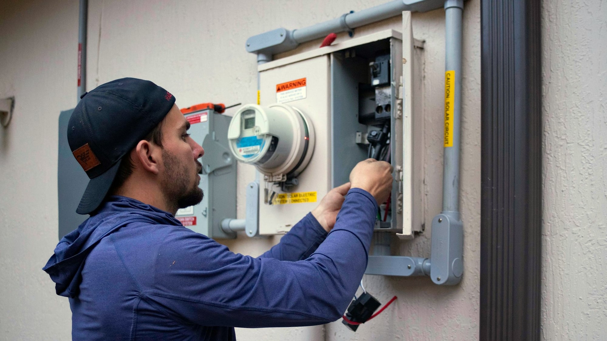 Man in cap working at outdoor electric meter and panel